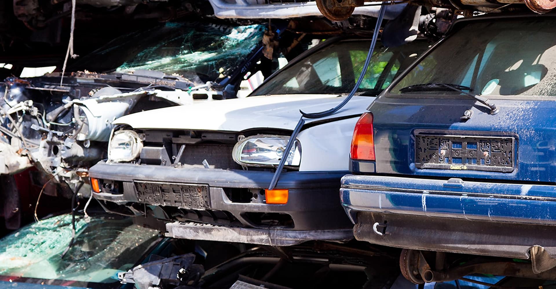 Gros plan sur des voitures accidentées et empilées dans une casse automobile, incluant une blanche à l'avant et une bleue à l'arrière.