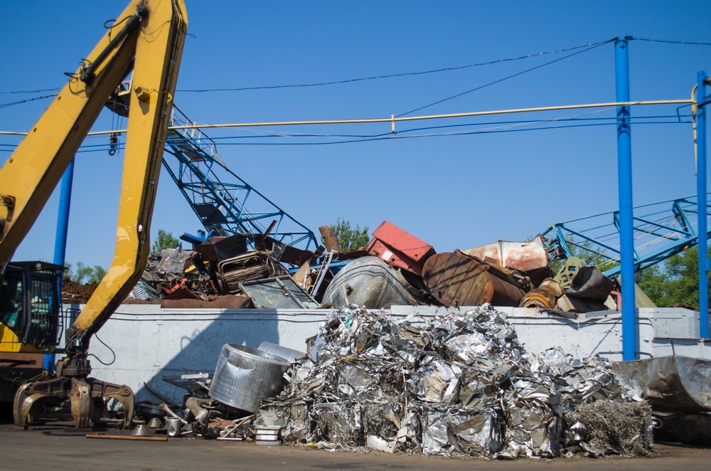 Recyclage de ferraille: La pelle mécanique charge les métaux. Excavatrice jaune chargeant des balles de ferraille compressée et des déchets métalliques variés dans une benne de recyclage industrielle.