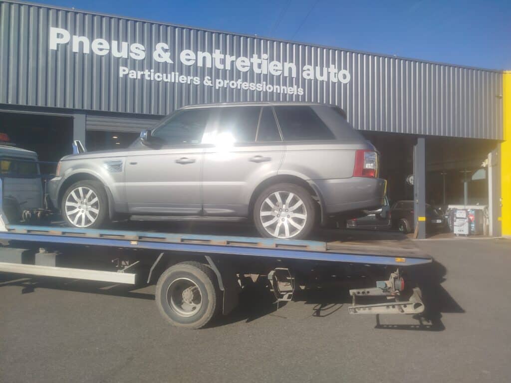 Pneus & Entretien Auto : Service pour Particuliers et Pros Range Rover Sport gris sur dépanneuse devant un centre "Pneus & entretien auto" pour particuliers et professionnels.