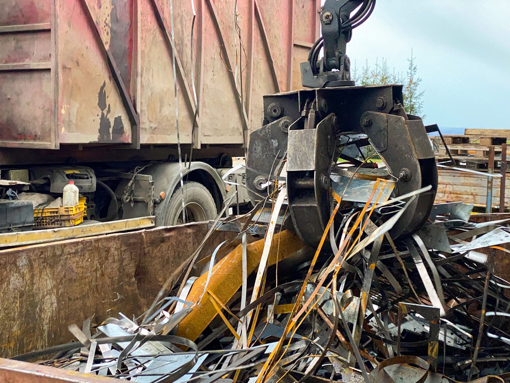 Ferraille et recyclage : un grappin charge la benne du camion. Grue hydraulique soulevant de la ferraille de métal découpé au-dessus d'une benne de recyclage à côté d'un camion.